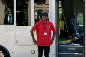 A Ride Connection driver in a red shirt stands smiling by an open Ride Connection bus.